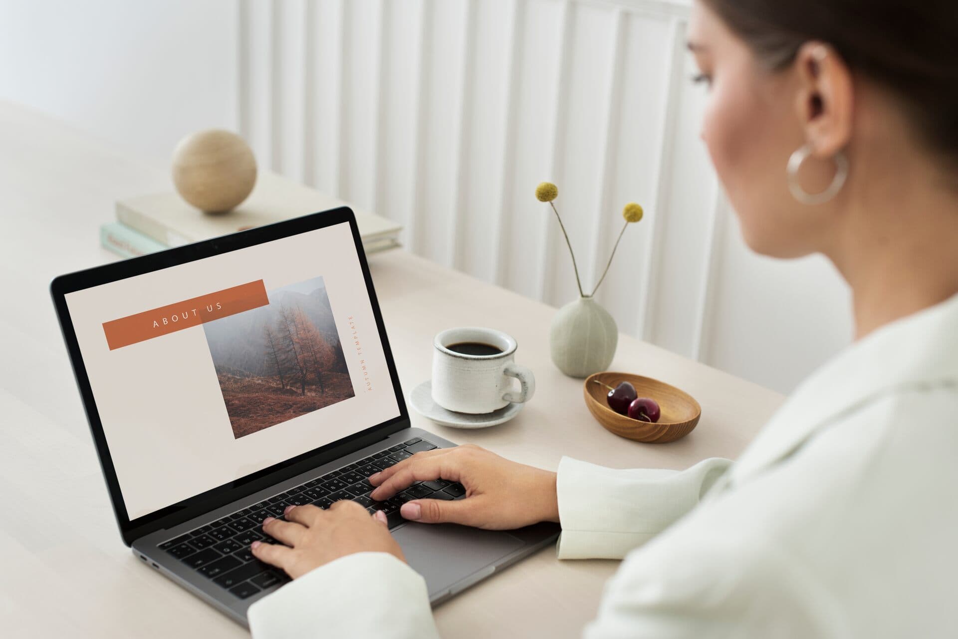 Mujer edita una página web en su laptop sobre un escritorio claro con café y flores
