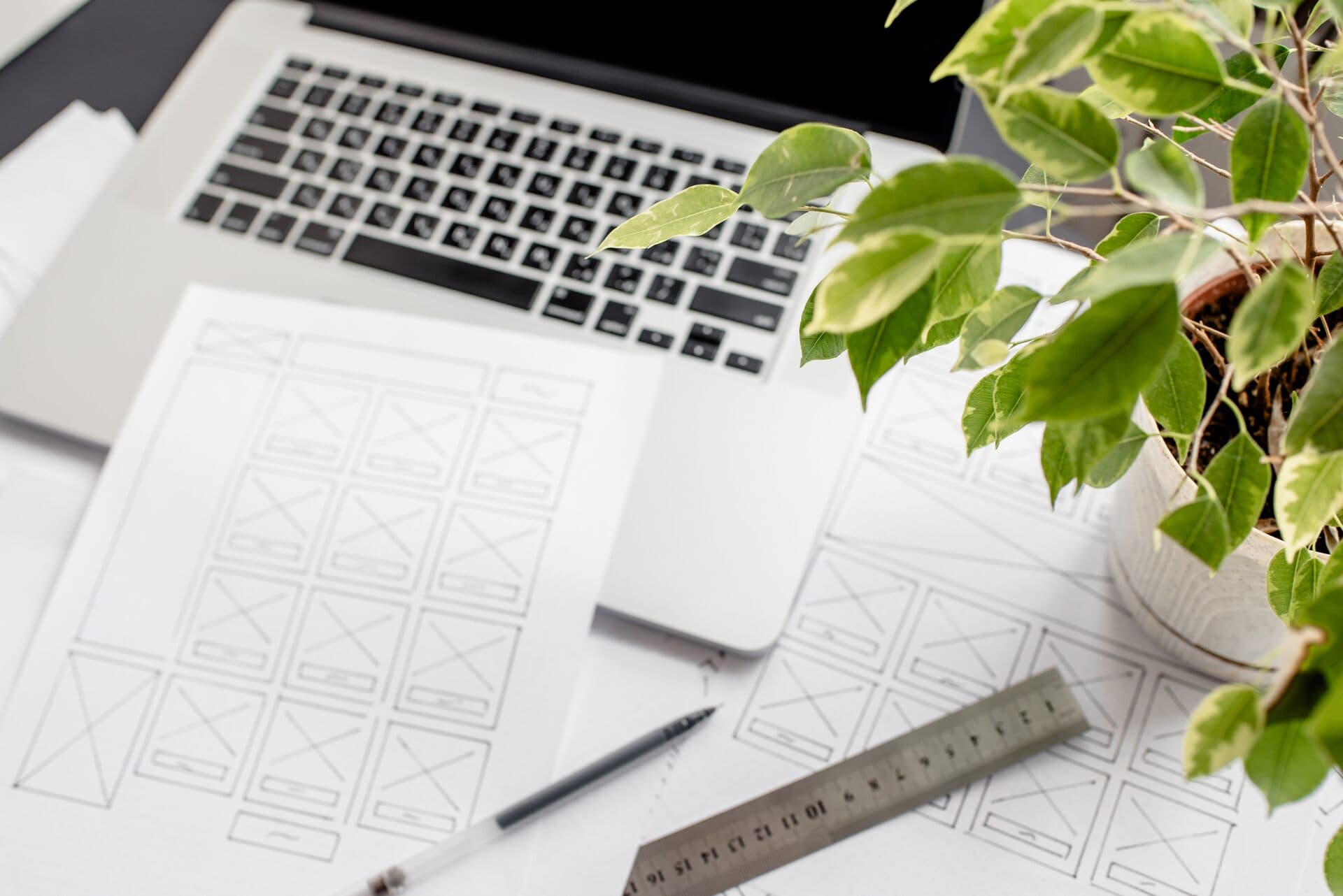 Bocetos a lápiz de la estructura de una página web junto a una laptop, regla y una planta