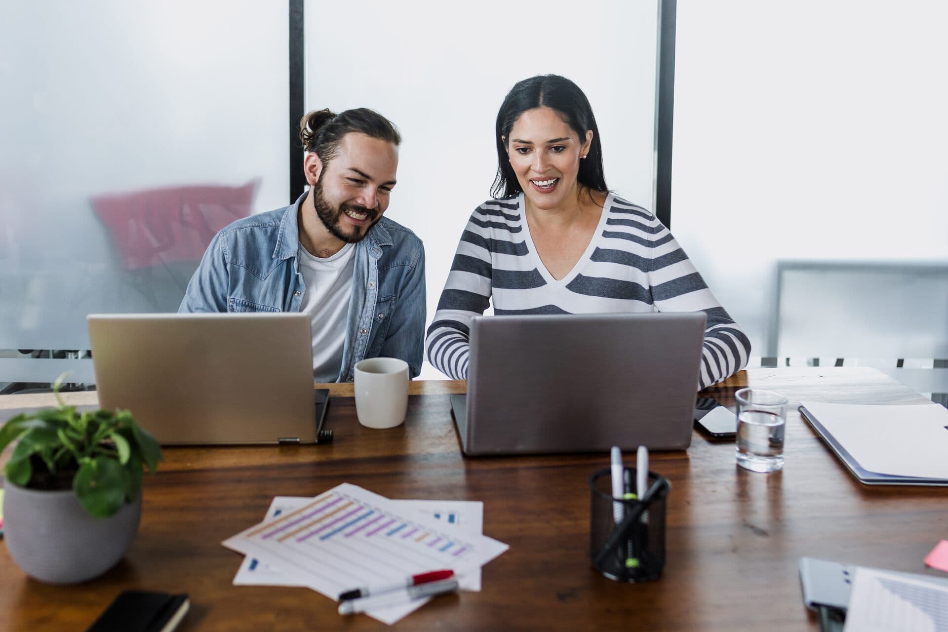 Dos emprendedores latinos conversan frente a sus laptops en una mesa de trabajo de una oficina en México