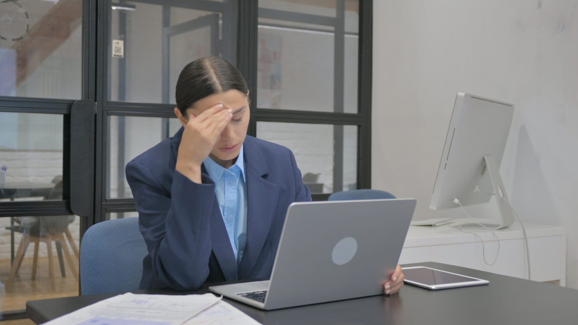 Worried businesswoman holds her forehead in front of her laptop